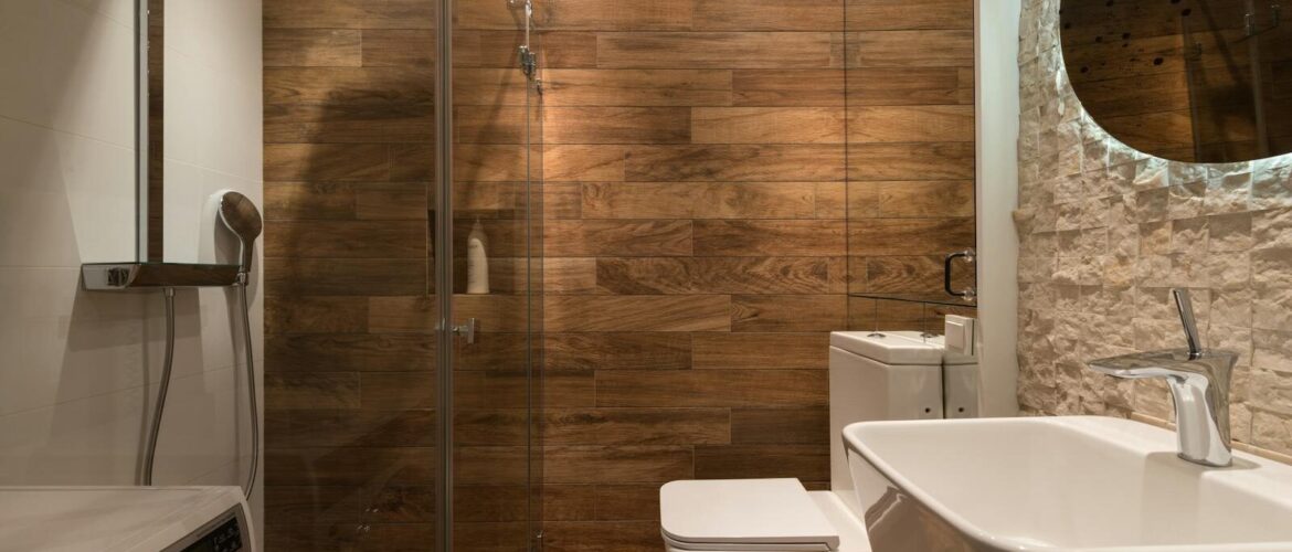 Stylish modern bathroom interior design with glass shower enclosure toilet bowl and sink under oval mirror