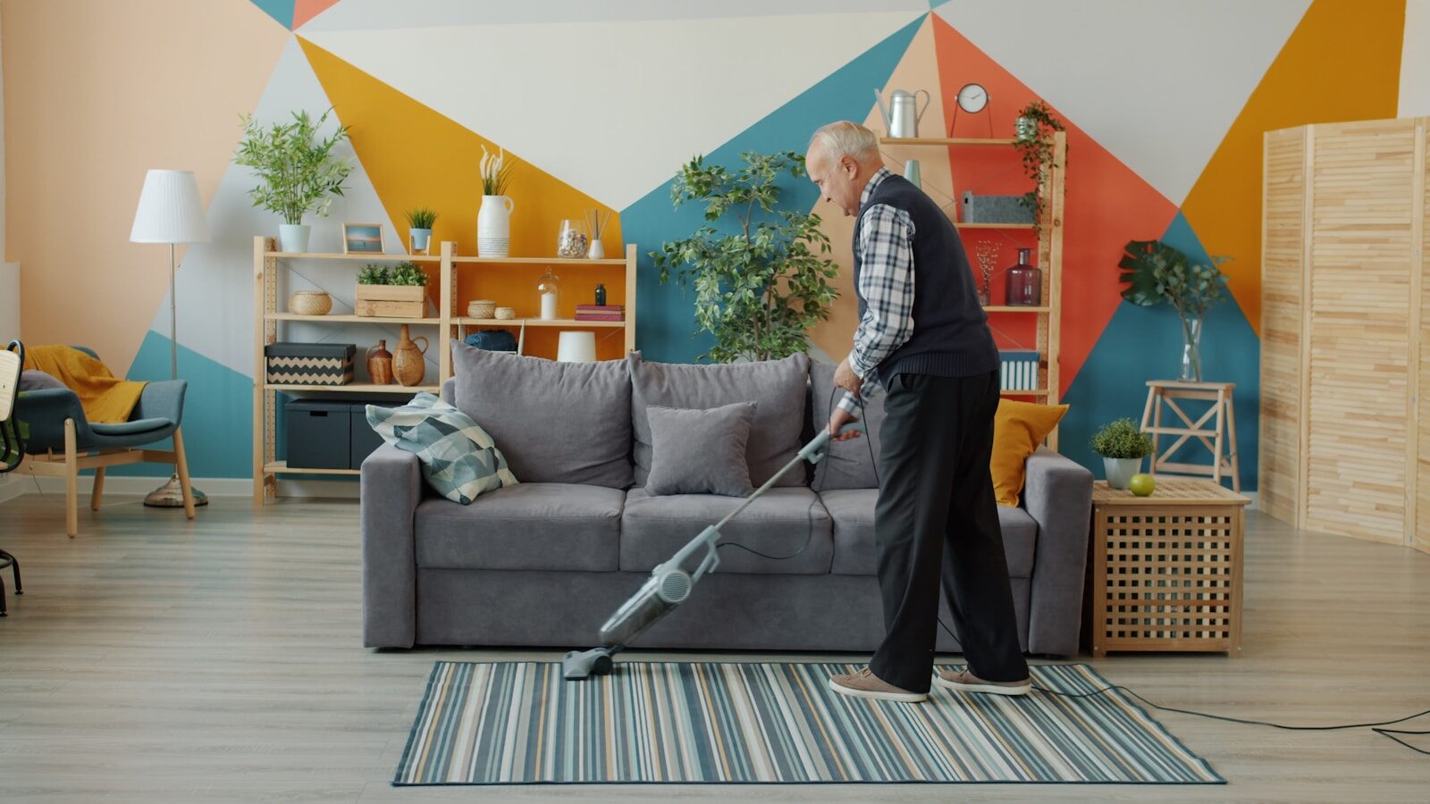 elderly woman vacuuming a colorful living room floor.