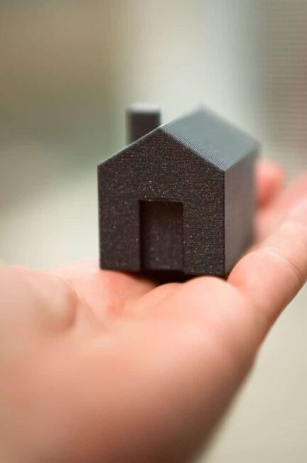 Close-up of a hand holding a miniature house model representing real estate concepts like buying or investment.